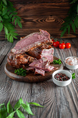 Smoked beef delicacy on a wooden background with herbs and leaves, with pepper and sea salt