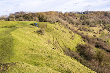 Hikers walking along the rampart of a slight univallate Iron Age hillfort on Ring Hill at the Cotswold viewpoint of Haresfield Beacon, Gloucestershire UK