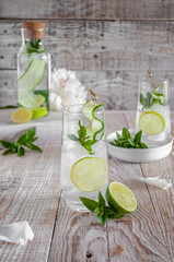 Obraz na płótnie Canvas Lemonade with ice, with lime, lemon and mint in a glass and a bottle decorated with cucumber on a skewer on a light background