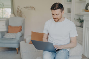 Serious young man using laptop computer for remote work from home