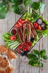 Grilled sausages on a tray with herbs, tomatoes, cucumbers, onions and herbs, sauce and flatbread on a light wooden background, for a large company.