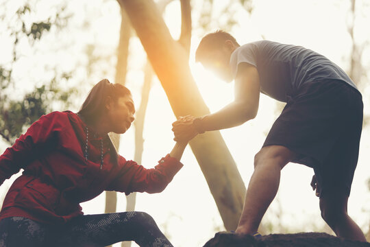 A young man is helping to pull a woman's hand to overcome obstacles.
