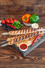 Kebab on skewers with baked pepper, basil, tarragon, fresh tomatoes and sauce on a brown wooden background