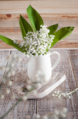Lilies of the valley in a white jug on a light wooden background