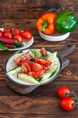 Cucumber and tomato salad with olive oil in a plate, on a wooden brown background with fresh tomatoes, peppers, chili