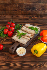 Wheat tortilla on a wooden board with tomatoes, pepper, herbs and sauce on a brown wooden background.