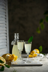 Lemoncello in a little glasses and bottle on a black background, Traditional Italian liqueur from lemons. Alcohol yellow and fresh lemon with green leaves on grey textured table. Copy space