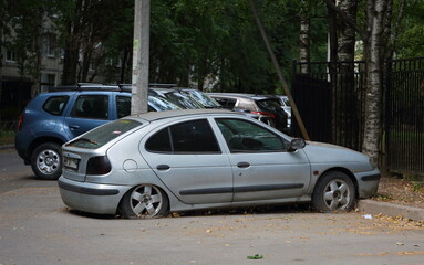 Naklejka premium An old gray rusty abandoned car with flat wheels in the courtyard of a residential building, ulitsa Podvoyskogo, St. Petersburg, Russia, July 2021