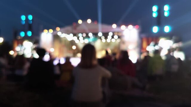 Girl sitting on a green field at a festival. Blurred image of people in a festival. Night lights