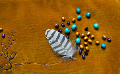 Striped bird feather, wooden beads and embroidery on a background of golden yellow velvet
