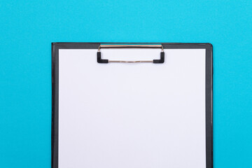 Black Clipboard with Blank White Sheet of Paper Lying on Blue Table - Top View, Flat Lay