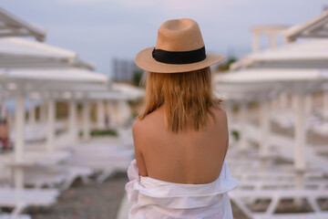 Healthy beautiful young woman stands on vacation in a straw hat and white shirt