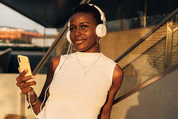 Cheerful and smiling African-American music-loving woman listening to her playlist songs using...