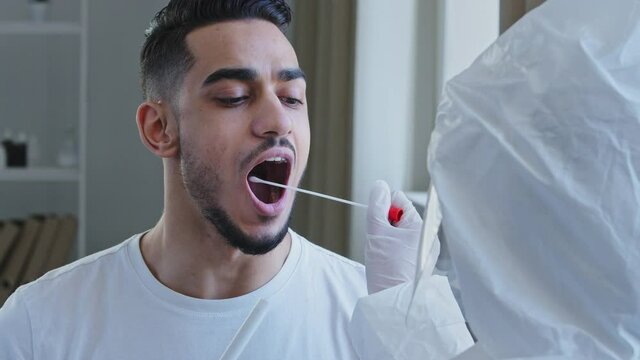 Close-up spanish man arabic male patient opens mouth donates saliva sample for infection virus, unrecognizable nurse medical worker doing pcr test with equipment for covid-19 coronavirus to ethnic guy