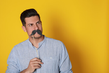 Man with fake mustache on yellow background. Space for text