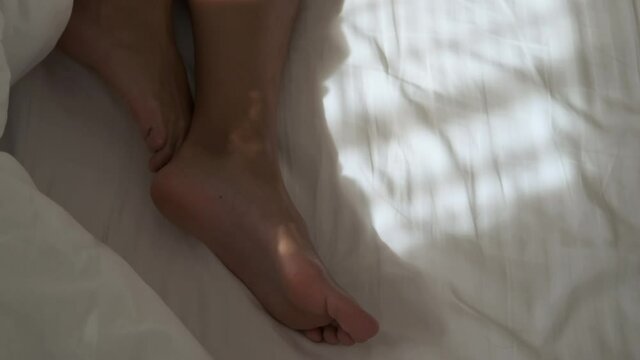 bare feet of woman sleeping on white bed linen in bedroom or in hotel room
