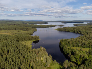 Bird's eye view of a lake with forest, blue sky with some clouds. Aerial, drone nature photography taken from above in Sweden in summer.  Copy space and place for text.
