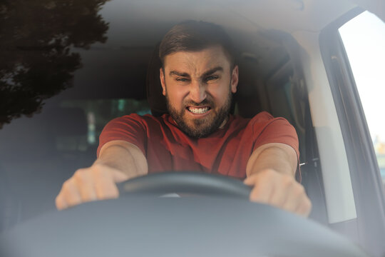 Emotional man in car, view through windshield. Aggressive driving behavior