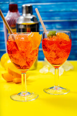 Vertical view of two glasses of the refreshing aperol spritz cocktail with mint and orange leaves. Selective focus.