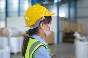 An engineering woman wearing medical mask , protective helmet working in warehouse factory