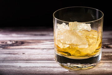 Chopped view of a glass with whiskey or scotch and large chunks of ice on a rustic wooden table.