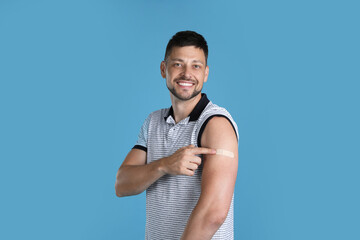 Vaccinated man showing medical plaster on his arm against light blue background