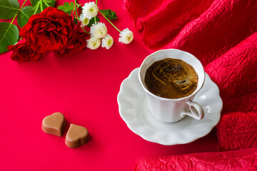 Coffee in a white cup, two heart-shaped candies and rose flowers. Romantic concept in dark red tones