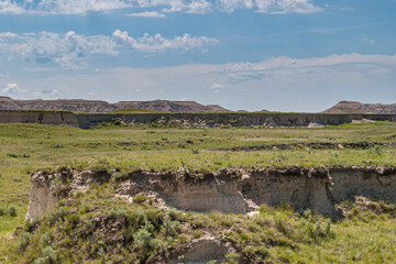 Badlands National Park, SD, USA - June 1, 2008: Closeup of small white-gray geologic table in green prairie with bigger such ridge on horizon under blue cloudscape.