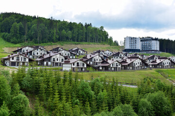 Fototapeta na wymiar Ski resort in summer with rows of low houses with brown roofs, against the backdrop of a bright blue sky and mountains