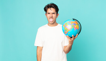young hispanic man feeling disgusted and irritated and tongue out and holding a world globe map