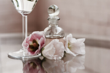 Essential aroma oil, serum or perfume in a little glass bottle with glass lid , flowers on glass table. Soft beige background. Copy space