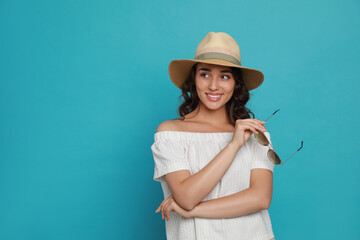 Beautiful young woman with straw hat and stylish sunglasses on light blue background. Space for text