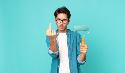 young hispanic man feeling angry, annoyed, rebellious and aggressive and holding a paint roller