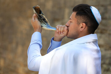 Jewish man in kippah and tallit blowing shofar outdoors. Rosh Hashanah celebration