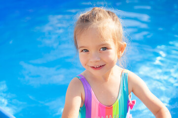 Fototapeta na wymiar Close-up Portrait of a laughing sweet girl in the pool. Bright swimsuit of rainbow color. Summer, swimming in the water. Beach, rest, vacation, heat