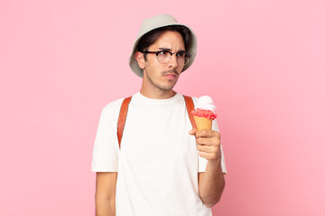 young hispanic man feeling sad, upset or angry and looking to the side and holding an ice cream