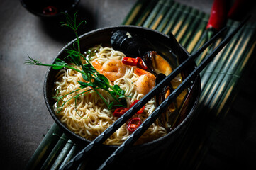Traditional Japanese soup ramen with shrimp, asian noodles, mussels chili pepper on dark background. Asian style food. Space for text. Noodles with seafood and microgreen