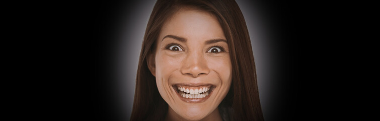 Scary face expression of crazy Asian girl with evil smile on black background banner. Woman smiling...