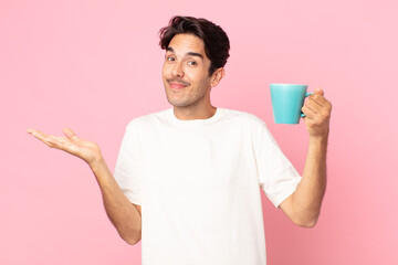 young hispanic man feeling puzzled and confused and doubting and holding a coffee mug