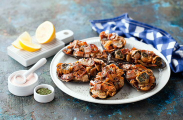 Large Grey baked mussels shells stuffed with fried bacon and mushrooms on a white plate