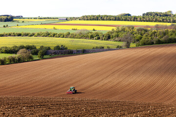 A tractor and seed drill sowing on Cotswold brash soil near the Cotswold village of Hampen, Gloucestershire UK - Powered by Adobe