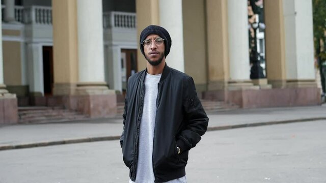 Serious handsome Arab with glasses and a hat looking at the camera in slow motion at the street