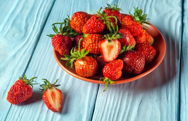 Full plate of strawberries and a cut piece on a blue table. Strawberry Diet Idea