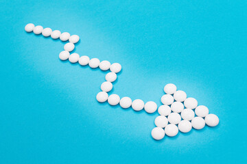 Fototapeta na wymiar Global Pharmaceutical Industry and Medicinal Products - Downward Arrow Made from White Pills on Blue Background