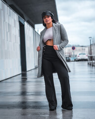 Obraz premium Street style in the city of a beautiful Latin girl with a leather hat and a gray raincoat walking in autumn
