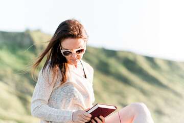Millennial adult young woman enjoying on the beach at sunset with a novel on vacation