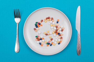 Global Pharmaceutical Industry and Medicinal Products - Different Colored Pills, Tablets and Capsules on Plate with Fork and Knife Lying on Blue Background, Top View, Flat Lay