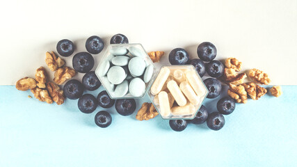 Various capsules with dietary supplements or vitamines, fresh blueberry and nuts