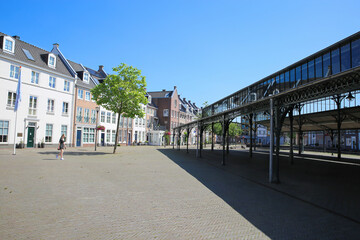 Naklejka premium Helmond, Netherlands - July 10. 2021: View beyond open market hall construction on square with traditional dutch houses in summer with blue sky
