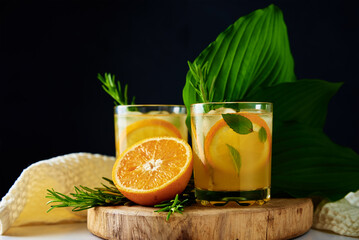 Lemonade with orange, rosemary and mint in glass on table. Summer fresh drink on dark background